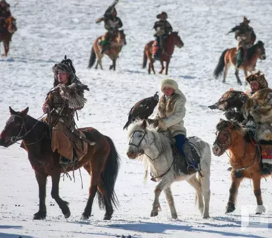 Eagle hunters riding horses across a snowy landscape in Mongolia.