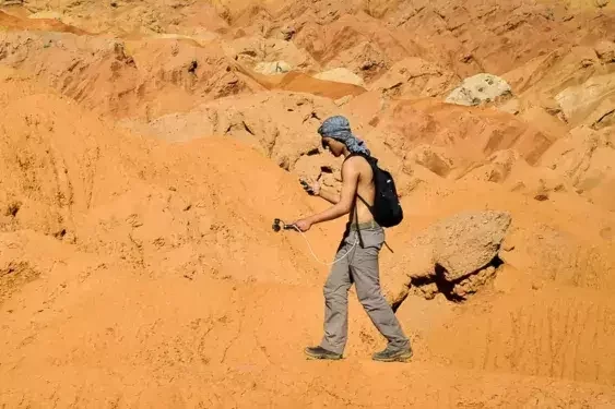 Hiker trekking through the Gobi Desert in Mongolia, walking across sandy terrain with backpack and hiking poles.