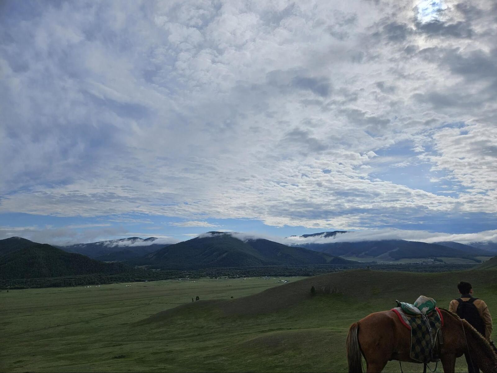 Horseback riding adventure travel in vast green valley with mountains and dramatic cloudy sky