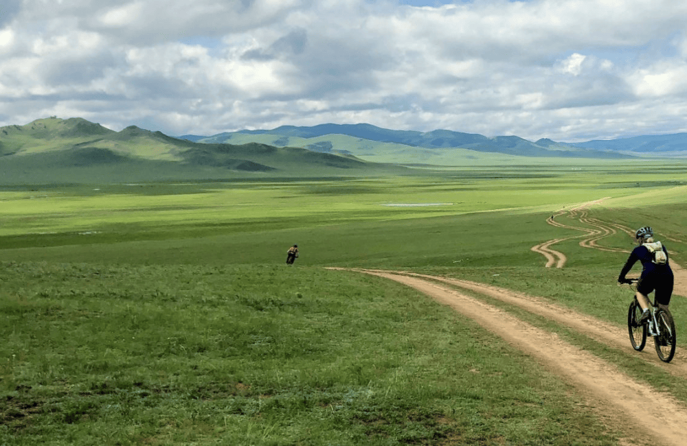 Cyclists riding across open steppe on off-road tours Mongolia scenic dirt trails and remote landscape