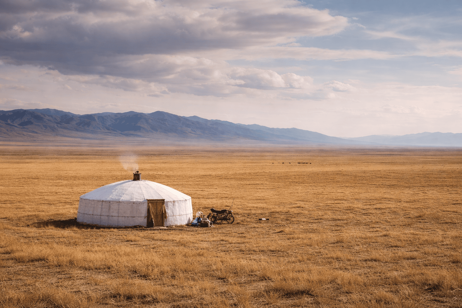 Traditional yurt on a vast Mongolian steppe with mountains in the distance under a cloudy sky