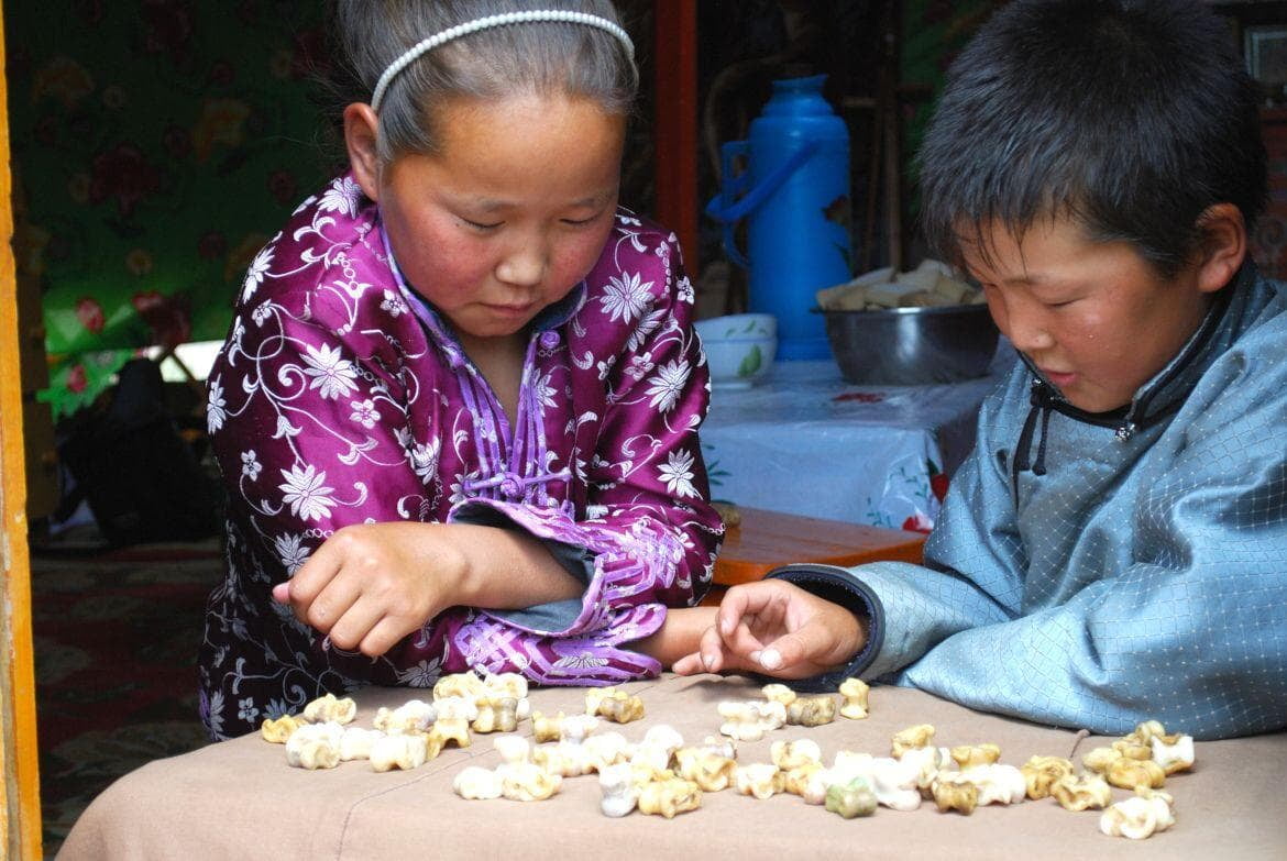 Nomadic Mongolian children playing traditional shagai ankle bone games during a Mongolia tour.