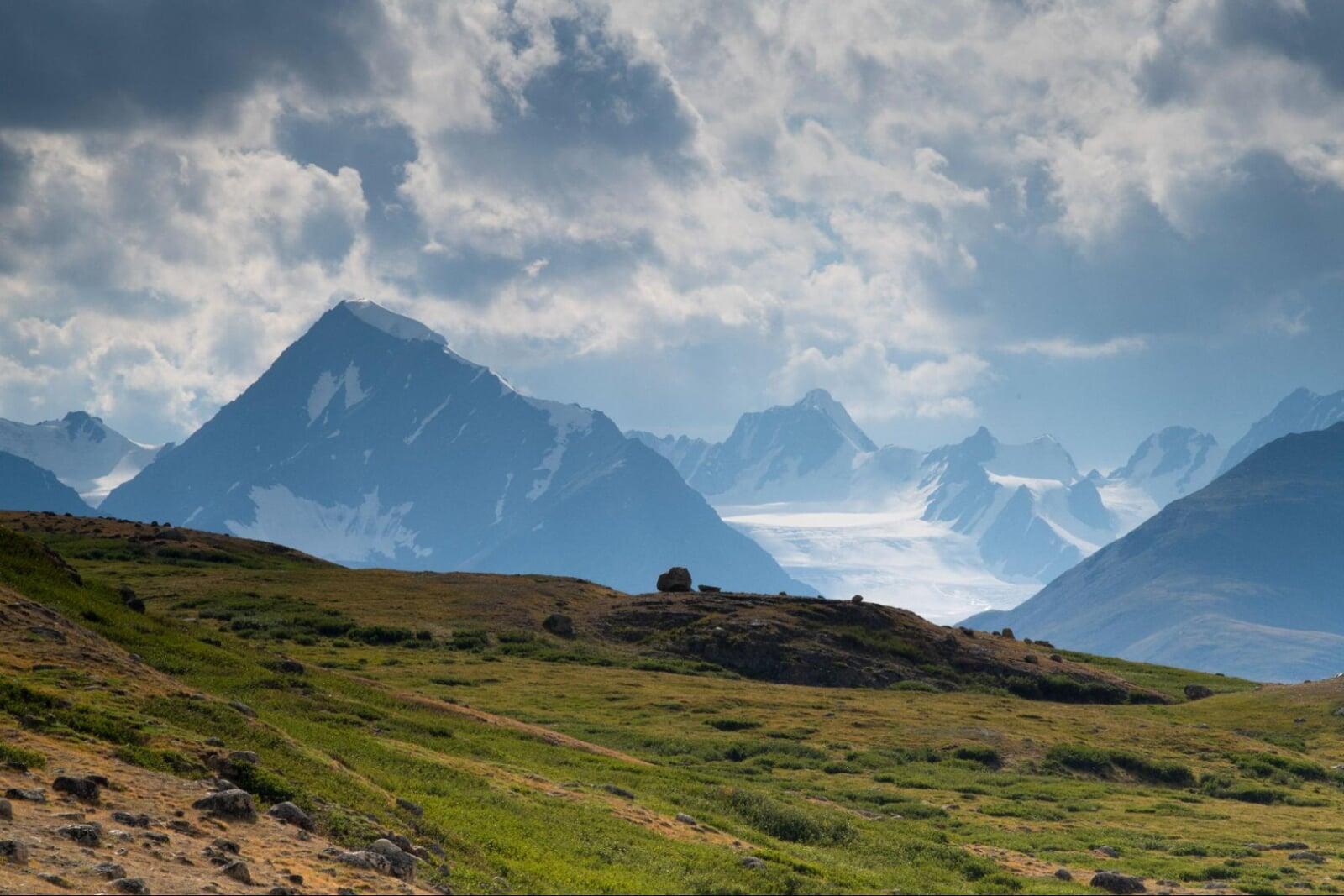 Remote mountain landscape in Mongolia with snow peaks and open grassland under cloudy sky