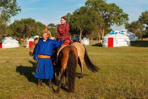 Adventure honeymoon in Mongolia featuring a couple enjoying a horseback experience beside traditional Mongolian gers in a peaceful countryside setting.