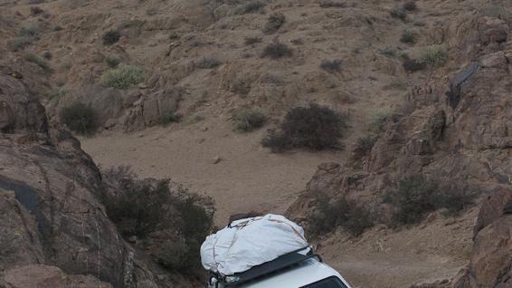 4x4 vehicle with roof cargo driving through a narrow rocky desert pass in Mongolia’s Gobi landscape.